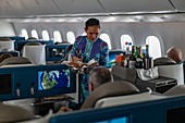 Flight attendant hands bread to passenger in Poerava Business Class aboard Air Tahiti Nui Boeing 787 Dreamliner aircraft on the flight from Paris Charles de Gaulle Airport (CDG) in France to Los Angeles International Airport (LAX) in the United States