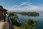 Young women overlook Lake Kivu from the terrace of the Emeraude Kivu Resort with the town of Bukavu in the Democratic Republic of the Congo in the distance, Cyangugu, Kamembe, Western Province, Rwanda, Africa