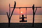 Silhouette of young woman on swing on Ong Lang Beach at sunset, Ong Lang, Phu Quoc Island, Kien Giang, Vietnam, Asia