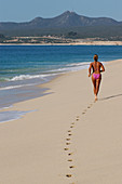A woman in a bikini jogging along the beach of the Sea of Cortez in Cabo San Lucas, Mexico.