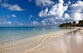 Morgens, ruhiger Strand menschenleer, ruhige Wellen und blauer Himmel mit weißen Wolken. Antigua