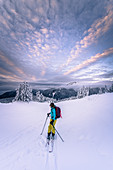 Person skiing through a wintry landscape, mountains in the distance, dramatic sky.