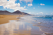Blick entlang eines Sandstrandes auf Fuerteventura an einem wolkigen Tag.