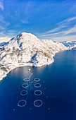 Luftaufnahme von schneebedeckten Bergen und Lachsfischfarm im arktischen Meer, Oksfjord, Loppa, Troms og Finnmark, Norwegen, Skandinavien, Europa