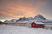 Die Holzhütte, umgeben von gefrorenem Meer und schneebedeckten Gipfeln bei Sonnenaufgang, Svensby, Lyngen-Alpen, Tromsø, Norwegen, Europa