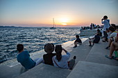 People gather along the seaside promenade to listen to the sea organ at sunset, Zadar, Zadar, Croatia, Europe