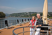 Paar auf Sonnendeck von Flusskreuzfahrtschiff während einer Kreuzfahrt auf dem Rhein, nahe Andernach, Rheinland-Pfalz, Deutschland, Europa