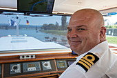 Kapitän auf der Brücke von Flusskreuzfahrtschiff  während einer Kreuzfahrt auf dem Rhein, nahe Andernach, Rheinland-Pfalz, Deutschland, Europa