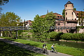 Cyclists on cycle path along the Tauber with the former Princely Court and White Tower of the city wall behind it, Wertheim, Spessart-Mainland, Franconia, Baden-Wuerttemberg, Germany, Europe