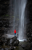 Mann mit roter Jacke am Wasserfall Fossa auf Insel Streymoy, Färöer Inseln\n