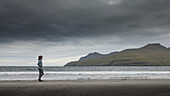 Woman runs in the sandy bay of Leynar on Streymoy, Faroe Islands