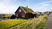 Schwarze Häuser mit roten Fenstern und Grasdach im Dorf Kirkjubøur auf Streymoy bei Sonne, Färöer Inseln\n