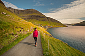Frau wandert bei Sonnenschein beim Dorf Bour auf Vagar, Färöer Inseln\n