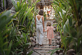 Mother and daughter holding hands on tropical resort boardwalk
