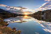 Sunburst über dem klaren Wasser des Sees Zana während des Sonnenaufgangs, Valmalenco, Provinz Sondrio, Valtellina, Lombardei, Italien, Europa