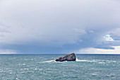 Rock island in front of Cap Frehel with rain clouds. Brittany, France