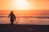 Surferin läuft im Sonnenuntergang zum Meer, Portugal
