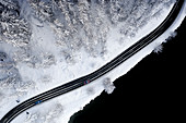 Autos fahren auf eisiger Straße durch verschneite Wälder am Rande des Sees Sils, Luftbild, Engadin, Kanton Graubunden, Schweiz, Europa