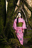 Portrait young woman in pink kimono in Japanese Noh mask at tree