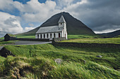 Dänemark, Färöer, Vidareidi, grüne Landschaft mit ländlicher Kirche und Berg