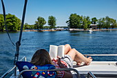 Junge Frau entspannt sich auf dem Sonnendeck von einem Le Boat Horizon Hausboot und liest ein Buch, Big Rideau Lake, Ontario, Kanada, Nordamerika