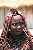 Angola; südlicher Teil der Provinz Namibe; Porträt einer Muhimba Frau; traditionelles Haarstyling; mit roter Erde verklebte Haarsträhnen und Fellpuschel; Halsreifen aus Leder; Haut mit roter Erde getönt