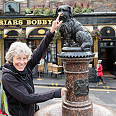 Woman rubbing nose at statue of Greyfriars Bobby Dogs memorial, Old Town Edinburgh, Scotland, UK