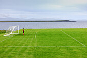 Lone goalkeeper, rural soccer field in front of the sea, Port Charlotte, Islay, Inner Hebrides, Scotland UK