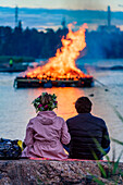 Paar schaut auf Feuer im See, Mitsommer Fest im Seurasaari Freilichtmuseum, Helsinki, Finnland
