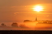Sunrise with a church in the fog in Neukirchen, Ostholstein, Schleswig-Holstein, Germany