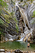 France, Alpes-de-Haute-Provence, Man in pond looking at waterfall on eroded rock