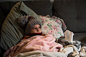 Canada, Ontario, Boy (8-9) in knit hat lying on sofa covered with blanket