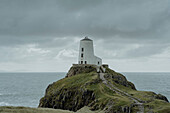 Lighthouse on ocean cliff under cloudy sky, Angelsey, Wales