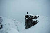 Hiker on remote snow covered cliff, Peak District National Park, England