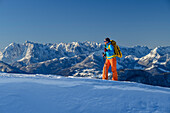Frau beim Wandern mit Schneeschuhen am Rucksack geht über Schneehang, Kaisergebirge im Hintergrund, Hochgern, Chiemgauer Alpen, Oberbayern, Bayern, Deutschland