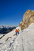 Man and woman hiking up to the Rotwand via snow slope, rock towers in the background, Rotwand, Spitzing area, Bavarian Alps, Upper Bavaria, Bavaria, Germany