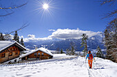 Frau beim Wandern geht über verschneiten Hang auf Gaststätte St. Martin zu, Kramerplateauweg, Garmisch, Ammergauer Alpen, Werdenfelser Land, Oberbayern, Bayern, Deutschland