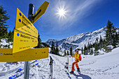 Woman on ski tour takes a break at the hiking sign, Großer Traithen, Mangfall Mountains, Bavarian Alps, Upper Bavaria, Bavaria, Germany