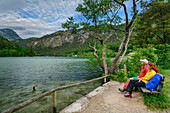 Man and woman while hiking sit on bench and look at Thumsee, Thumsee, Berchtesgaden Alps, Salzalpensteig, Upper Bavaria, Bavaria, Germany