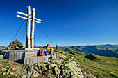 Frau beim Wandern sitzt an Gipfelkreuz, Falkert, Nockberge, Nockberge-Trail, UNESCO Biosphärenpark Nockberge, Gurktaler Alpen, Kärnten, Österreich