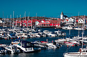 Hafen und rote Häuser mit Kirche im Dorf Skärhamn auf der Schäreninsel Tjörn an der Westküste von Schweden, blauer Himmel mit Sonne\n