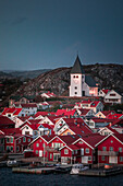 Rote Häuser mit Kirche im Dorf Skärhamn auf der Schäreninsel Tjörn an der Westküste von Schweden, am Abend\n