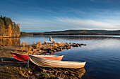 Frau und Boote am See in Lappland in Schweden bei Sonne mit blauem Himmel\n