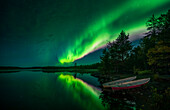 Northern lights in the night sky on the lake shore with boats in Lapland, Sweden