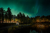 Camping mit VW Bulli Campervan unter Polarlichtern im Nachthimmel am Seeufer in Lappland, Schweden\n