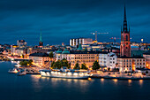 Beleuchtete Skyline von Stockholm bei Nacht mit Kirche Riddarholmskyrkan auf Altstadtinsel Gamla Stan in Schweden\n
