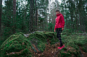 Woman hikes over mossy rocks through forest in Tyresta National Park in Sweden