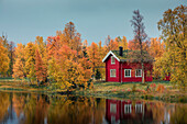 Rotes Haus am See im Herbst entlang der Wilderness Road in Lappland in Schweden\n