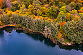 Herbstliche Luftaufnahme eines bunten Waldstücks an einem blauen See in Hessen, Deutschland
