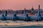 Icy old wooden pier on the beach at sunrise, in the background pier light (lighthouse), Travemünde, Bay of Lübeck, Schleswig Holstein, Germany